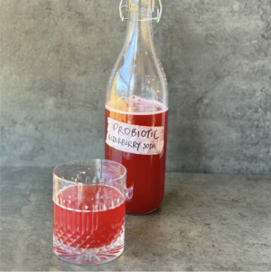 a photo of a glass of elderberry soda with a glass bottle